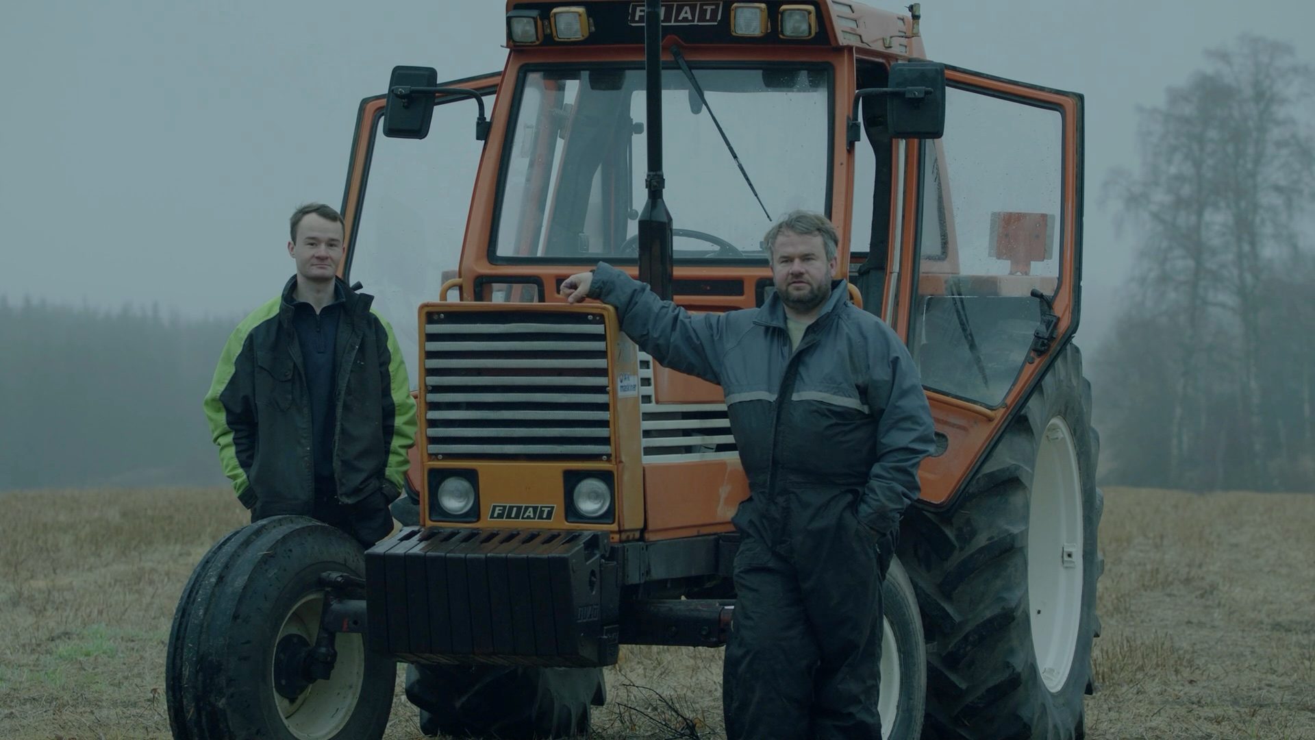 To personer står ved en oransje traktor på et jorde