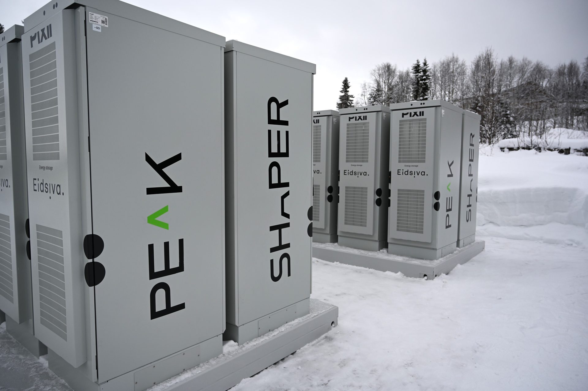 Grey energy storage units by PIXII, PEAK, and Eidsiva in a snowy landscape with trees.