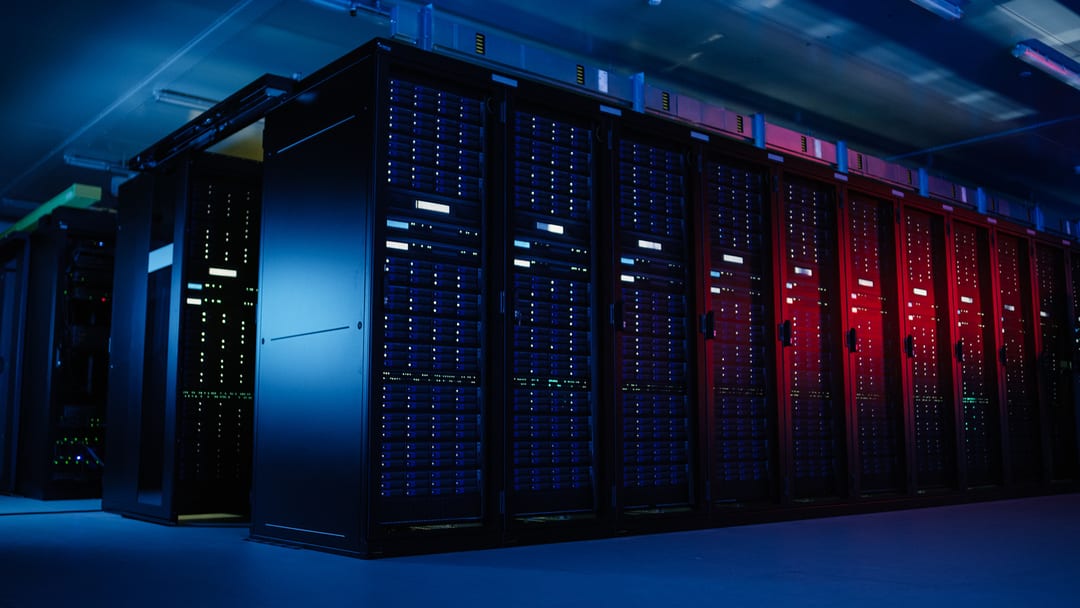 Bildet viser innsiden av et datasenter med lange rekker av servere stablet i høye rack. Serverne har blinkende lys og er koblet med mange kabler. Atmosfæren er kjølig og teknisk.